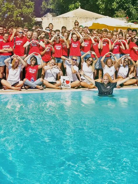 Large group of Sprachcaffe junior students in Malta posing by the poolside, many forming heart shapes with their hands.