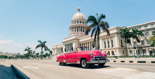 Klasyczny samochód przejeżdża przed budynkiem Kapitolu w Hawanie, Kuba, łącząc historyczny urok z tropikalnym klimatem miasta.