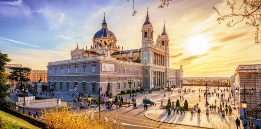 Malowniczy zachód słońca nad Katedrą Almudena w Madrycie, Hiszpania, tworząc ciepłą i przyjazną atmosferę na placu pełnym spacerujących ludzi.