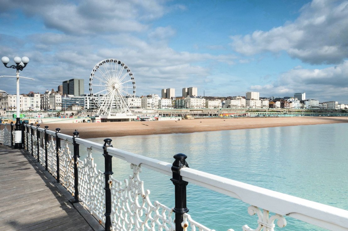 Panorama nadmorskiego miasta Brighton z widokiem na słynne molo Brighton Pier oraz diabelski młyn, oferująca malowniczy krajobraz plaży i rozrywek miejskich.