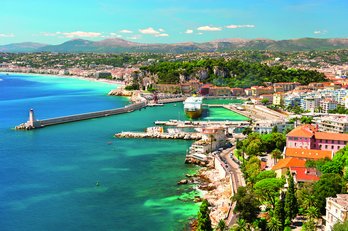 **ALT:** Widok z lotu ptaka na malowniczą Niceę, Francja, z turkusowymi wodami Morza Śródziemnego, portem i zabudową miejską otoczoną zielenią.