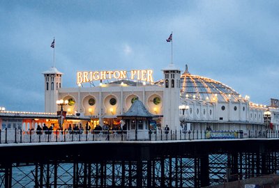 Brighton Pier o zmierzchu, widok na oświetlone molo z charakterystyczną kopułą, otoczone niebieskim niebem i morzem