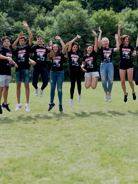 Sprachcaffe students in England jumping mid-air on a green field, wearing matching shirts and enjoying the outdoors.