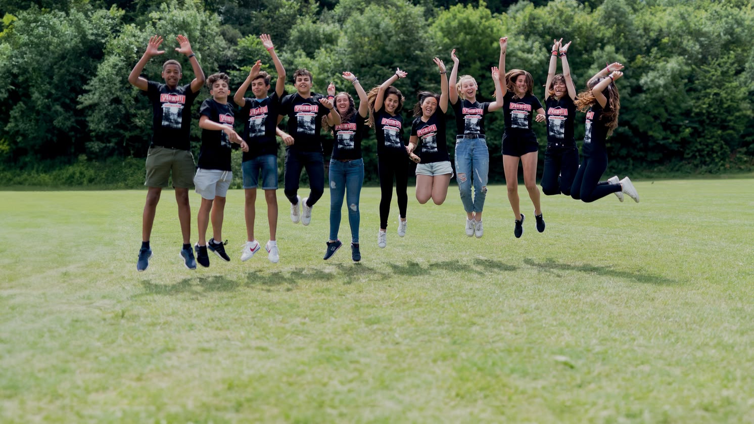 Sprachcaffe students in England jumping mid-air on a green field, wearing matching shirts and enjoying the outdoors.