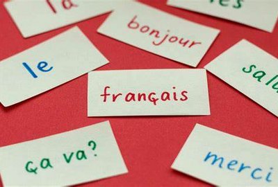 **ALT:** Kartki z francuskimi słowami i zwrotami, takimi jak "français," "bonjour," "le," "ça va?," i "merci," rozłożone na czerwonym tle.